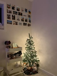 a small christmas tree sitting in the corner of a room with pictures on the wall