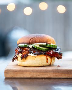 a bbq sandwich sitting on top of a wooden cutting board with cucumbers