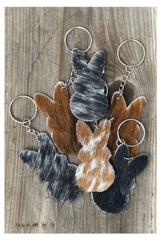 four keychains with different colors and shapes on wooden surface, one has an animal head