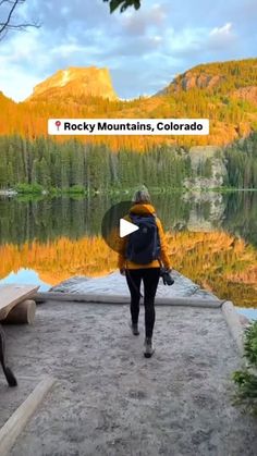 a person with a backpack walking towards a body of water and mountains in the background