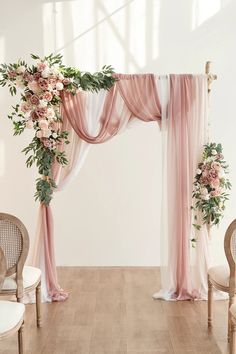 the wedding arch is decorated with pink flowers and greenery, along with white drapes