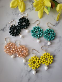 six pairs of beaded earrings sitting on top of a marble table next to yellow flowers