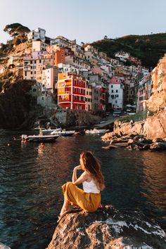 a woman sitting on top of a rock next to the ocean in front of a city