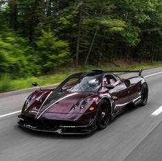 a maroon sports car driving down the road with trees in the backgrouund