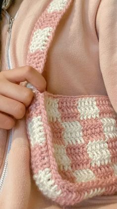 a close up of a person holding a crocheted bag in their hands and wearing a pink sweater