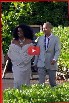 a man and woman dressed in formal wear walking through some bushes with one holding the other's hand