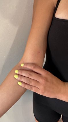 a woman's hand with yellow nail polish holding onto her arm and wearing a black tank top