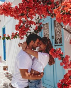 a man and woman embracing in front of a blue door with red flowers on it