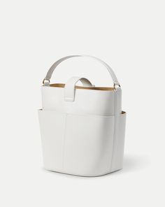 Defined by its sculptural shape, the Crest Lock Bucket bag is an everyday hero. It’s distinct yet understated design gives it maximum versatility while its relaxed yet sleek look feels of-the-moment. It’s crafted from supple leather and finished with minimalist hardware, including a crest-engraved lock closure. Its luxurious suede interior is finished with a generous flat pocket, while it’s four-compartment exterior allows for further organization. Can be carried as a top handle, crossbody or sh White Bucket Bag With Double Handle And Adjustable Strap, White Bucket Bag With Adjustable Strap And Double Handle, White Leather Bucket Bag For On-the-go, White Bucket Bag With Adjustable Strap For On-the-go, White Leather-handled Bucket Bag, Jacket Store, Everyday Heroes, Leather Bucket, Leather Bucket Bag