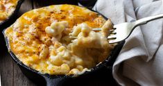 a skillet with macaroni and cheese in it on a table next to a fork