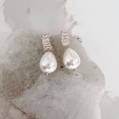 a pair of pearl and diamond earrings sitting on top of a rock