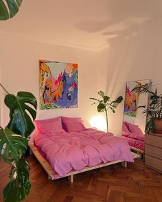 a bedroom with pink bedding and paintings on the wall, wooden flooring and potted plants