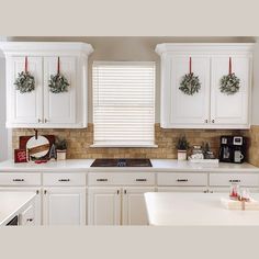 a kitchen with white cabinets and christmas wreaths on the windowsill