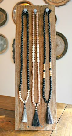 three beaded necklaces with tassels hanging on a wooden board in front of pictures