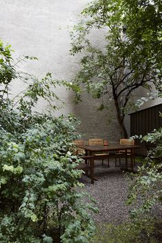 there is a table and chairs in the woods by the house with no one around it