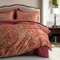 a bed with red and gold comforters in a room next to a window,