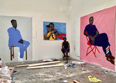 two men sitting in front of paintings on the wall and floor with construction materials around them