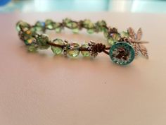 a bracelet with green glass beads and a flower charm on it's end, sitting on a table