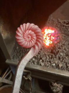 a pink flower sitting on top of a piece of metal in front of a fire