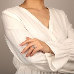 a woman with her arms crossed wearing a white shirt and diamond ring on her left hand