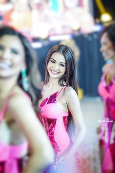 a woman in a pink dress standing next to another woman with long dark hair and smiling