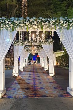 an outdoor wedding ceremony with white drapes and flowers on the aisle, decorated with chandeliers