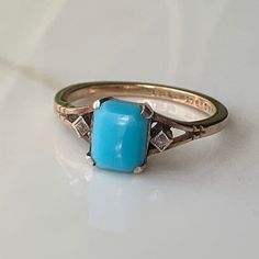 a gold ring with a turquoise stone in the center on a white surface, it is surrounded by small diamond accents