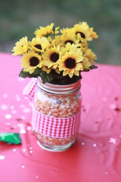 sunflowers are in a mason jar on a pink table with confetti