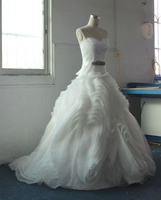 a white wedding dress is on display in front of a blue table and windowsill