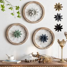 three circular metal wall hangings on a white wall above a wooden table with flowers