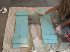 a woman is painting wooden shutters with blue paint