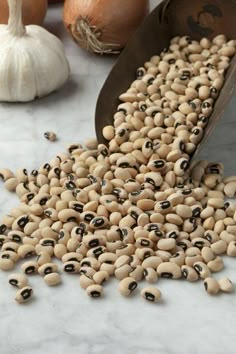 a pile of beans sitting on top of a table next to onions and garlics