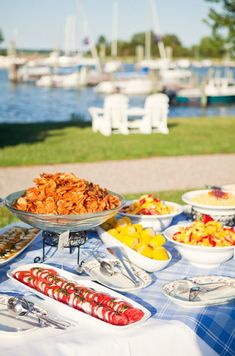 a table full of food with boats in the water and grass on the other side