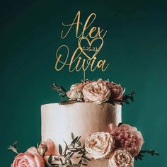 a wedding cake with pink flowers and gold lettering that says alex & aliya on top