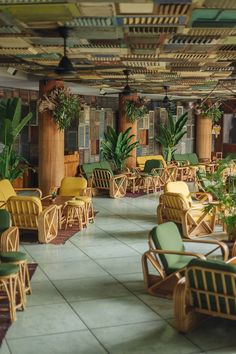 an indoor seating area with green chairs and potted plants on either side of it