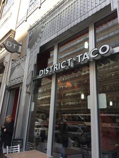 people are walking past a restaurant called district taco