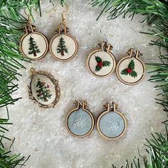 six christmas ornaments hanging from a tree branch on top of snow covered ground with pine needles