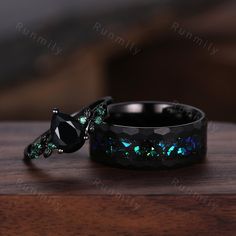 two black rings with green and blue crystals on them sitting on a wooden table next to each other