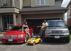 two people standing next to their cars in front of a house