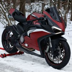 a red and black motorcycle parked on the side of a snow covered road next to trees