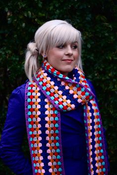 a woman with blonde hair wearing a blue shirt and colorful crochet scarves