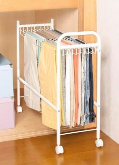 a white rack with clothes on it in front of a wall and a dresser next to it