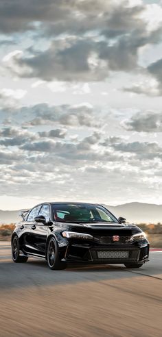 a black car driving down a road under a cloudy sky with clouds in the background