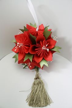 a bouquet of red paper flowers sitting on top of a white table with a tassel