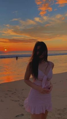 a woman standing on top of a sandy beach next to the ocean at sun set