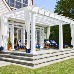 a white pergolan covered patio with blue chairs on the steps and green grass