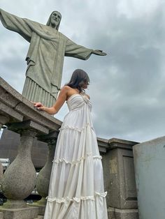 a woman in a white dress standing next to the statue of jesus on top of a hill