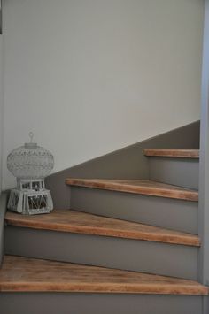 a white birdcage sitting on top of some wooden steps next to a wall