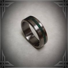 a wedding ring with green and black stripes on the inside, sitting on a white surface