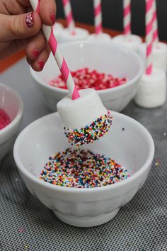 a person holding a marshmallow with sprinkles on it in a bowl